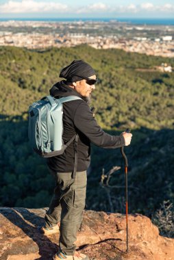 Orta yaşlı bir adam, Garraf Doğal Parkı 'nın manzaralarını incelerken bir dağın eteklerinde yürüyor..