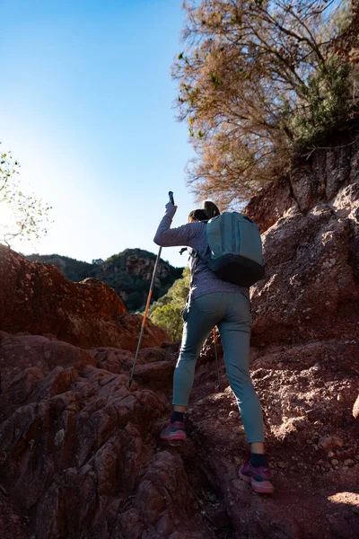 Woman climbs the mountain in the Garraf Natural Park, supported by hiking sticks.