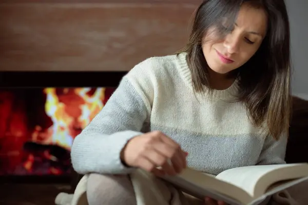 Woman drawn to the story of a book in the comfort of her home.