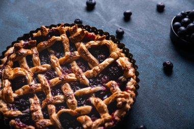 Kırmızı meyve ve yaban mersinli turta koyu mavi arka planda sunuluyor..