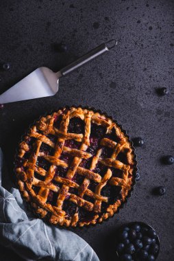 Ev yapımı kırmızı meyve ve yabanmersinli turta koyu bir arka plana yerleştirilip yukarıdan izleniyor..