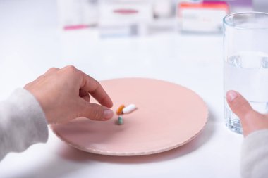Tabakta haplar ve bir bardak suyla tedavi edilmek üzere olan birinin elleri..