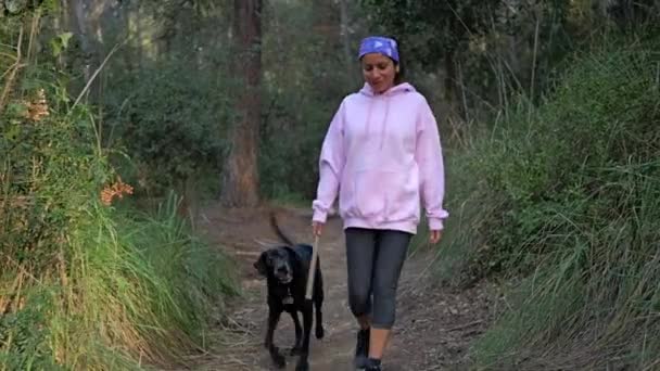 高齢の犬と一緒に狭い森の道を歩いている女性 — ストック動画
