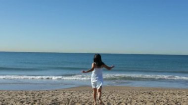 Kadın denize doğru koşar ve sahilde ayaklarını ıslatır.