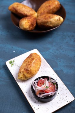 İçinde tuzlu dolgu olan çıtır bir patates ve yanında da soğan ve domates salatası..