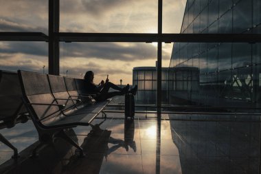 Güneş gökyüzündeki bulutların arasından yükselirken kadın havaalanında uçuşunu bekliyor..