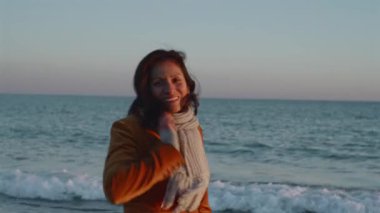 Resmi giyinmiş bir kadın kameraya bakıyor ve denizde yürürken gülümsüyor..
