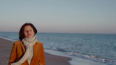 Bir kadın sahilde yürürken gün batımının ışınlarını alır..