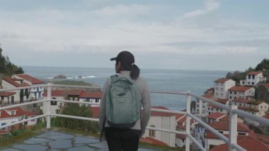 Sırt çantası ve spor kıyafetleri olan bir kadın İspanya 'nın ünlü Cudillero kasabasında bir bakış açısına doğru yürür..