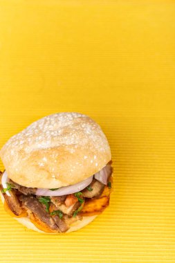 Sarı arka planda domuz eti ve soğan parçaları olan Perulu sandviç..