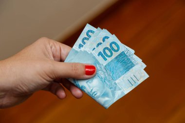 Birkaç yüz gerçek banknot. Brezilya 'dan gelen para kırmızı tırnaklı bir kadının elinde.