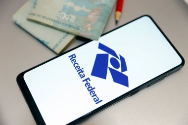 Minas Gerais, Brezilya - 28 Eylül 2023: Brezilya Federal Gelirli akıllı telefon ekranı ve birkaç Brezilyalı reel banknot