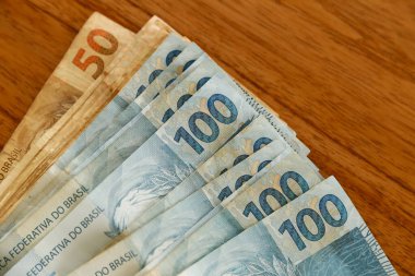 Brezilya 'da finans, ekonomi ve zenginlik temaları için mükemmel olan, 100 Brezilyalı gerçek banknota odaklı kırsal ahşap masaya yayılmış çeşitli faturalar.