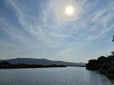 Yumuşak, ince bulutlardan oluşan engin bir gökyüzünün altında dolambaçlı bir nehri olan sakin bir manzara. Bereketli bitki örtüsü kıyılarda, huzurlu ve sakin bir açık hava ortamı öneriyor, doğada rahatlama ve keşif için mükemmel..