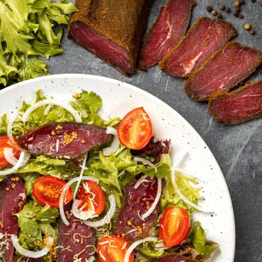 Unusual tasty dish with Dried beef or pork basturma and tomatoes, onion, lettuce, Coriander leaves, cheese. Armenian national snack. Top view, concept for menu or ingridient