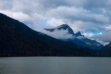 Bulutlar ve Huzur: Bir Dağ Gölü Bulutlu Sonbahar Gökyüzünü Yansıtır, Misty Alpine Peaks ile çevrilidir. Yüksek kalite fotoğraf