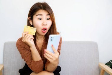Heyecanlı alışverişçi Asyalı kadın, elinde kredi kartı ve cep telefonu ile satış ürünleri için ödeme yapmaya hazır.