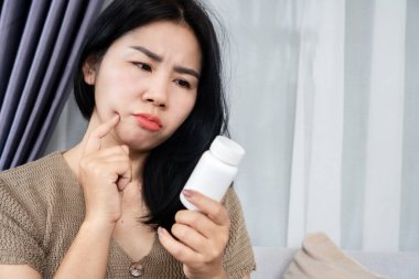 prioritizing safety concept with an asian woman reads a drug label on a bottle before taking medication clipart