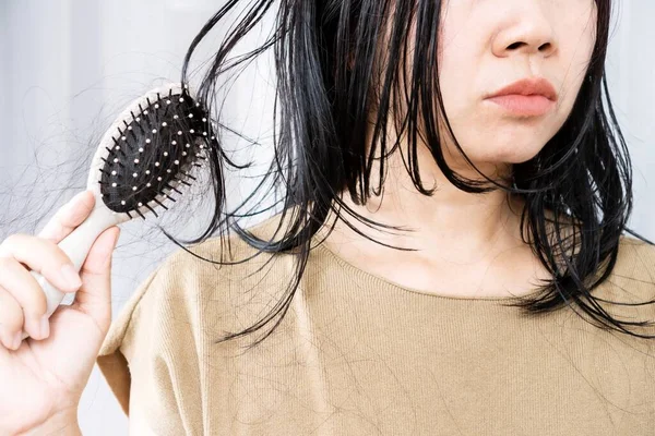 Asian woman experiences hair loss while brushing wet hair with a comb