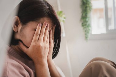 Stresli Asyalı bir kadının yalnız başına oturup yüzünü örttüğü akıl sağlığı konsepti.
