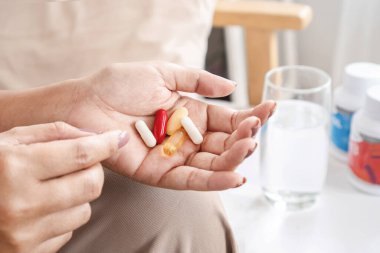 Kadın eli ek gıda, vitamin C, B vitamini, balık yağı, bir şişe ilaç ve bir bardak su alıyor.