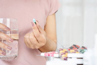 Yakın plan kadın eli bir bardak suyla antibiyotik hapı alıyor.