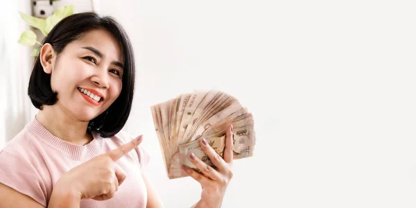Szczęśliwa Azjatka Trzymająca Pieniądze Wskazujące Tajskie Banknoty Uśmiechniętą Twarzą — Zdjęcie stockowe