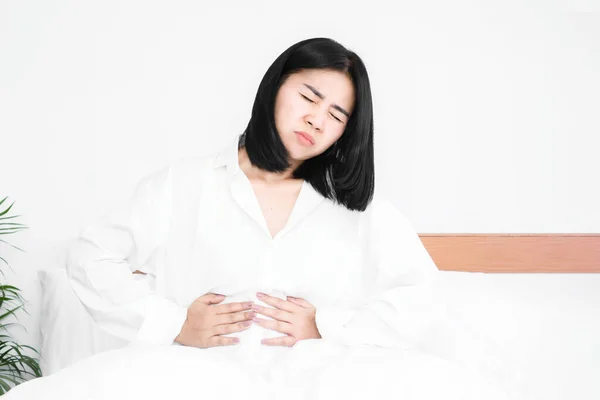 アジアの女性は 胃の痛みに苦しんで ベッドに座って — ストック写真