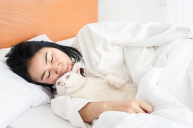Yatakta kediyle uyuyan Asyalı kadın.