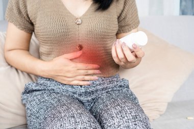 Karın ağrısı çeken, ishal olmuş, elinde ilaç şişesi tutan bir kadın.