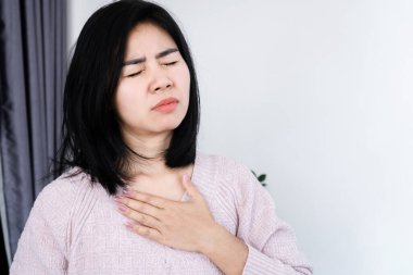 Asyalı kadın kalp krizi geçiriyor, göğüs ağrısı, nefes almakta zorlanıyor.