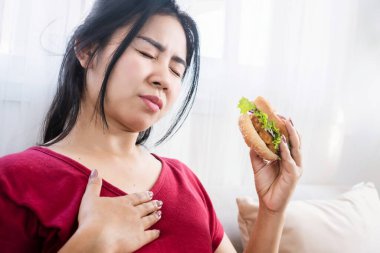 Asyalı kadın mide ekşimesi, hamburger yedikten sonra reflü, abur cubur konsepti yiyor.