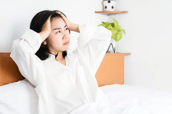 stock image Asian woman having a problem with depression sitting in bed hand holding her head, overthinking and bad feeling