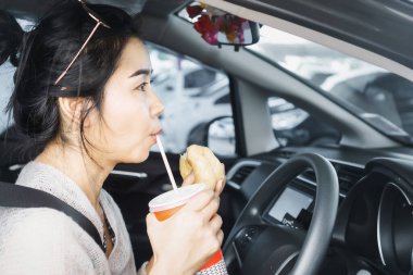 Meşgul Asyalı kadın fast food yiyor ve arabada kahve içiyor.