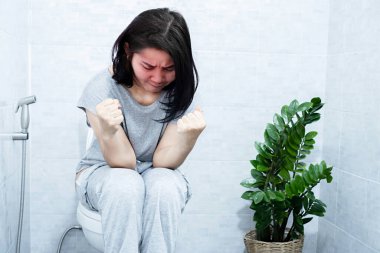 Kronik kabızlık konsepti. Asyalı bir kadın tuvalette oturuyor. Sert dışkılar ve bağırsak hareketlerinin yumru yumru yumru ve zor bir geçişi var.