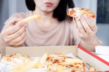 Aşırı pizza yiyen Asyalı kadın ve patates kızartması, sağlıksız yaşam tarzı, aşırı yeme bozukluğu konsepti.
