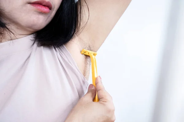 asian woman shaving armpits to remove hair underarm by using razor