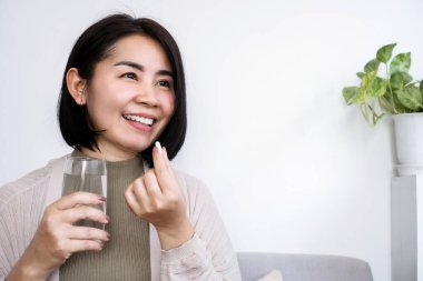 healthy Asian woman taking probiotic supplement pill with a glass of water  clipart