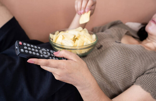 расстройство питания, нездоровое питание соленая закуска с женщиной лечь с картофельными чипсами и дистанционного телевидения в руках 