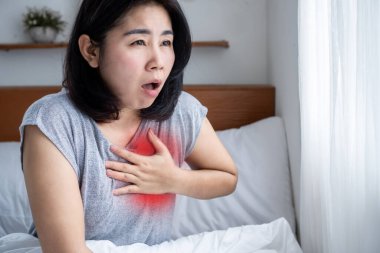 Coronary artery disease CAD concept with asian woman suffering from chest pain, shortness of breath and heart attack in bed clipart