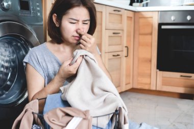 Asian housewife woman unhappy with bad stinky smelling clothes after washing, smelly laundry concept clipart