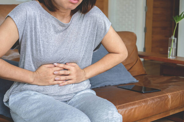Asian woman suffering from stomach pain, stomachache chronic due to irritable bowel syndrome or IBS, digestion system problem