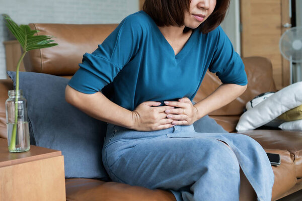 Asian woman suffering from stomachache, feeling pain during menstruation , can be used for diarrhea, food poisoning concept 