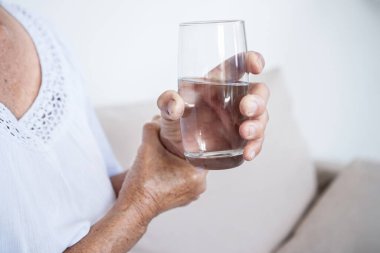 Parkinson hastası yaşlı bir kadın sinir sistemi düzensizliğinden kaynaklanan kontrol edilemeyen el titremelerinden dolayı bardaktan su içmeye çalışıyor.