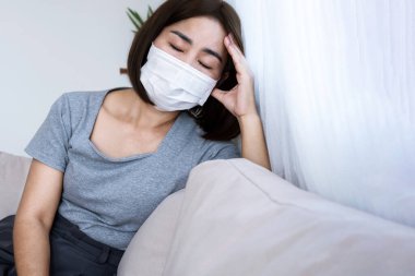 Maske takan Asyalı kadın, yüksek ateş, baş ağrısı ve soğuk gibi Coronavirüs belirtilerinden muzdarip. COVID-19 karantina kavramı