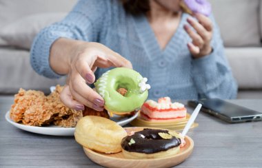 Kadınların elleri masaya uzanıp kızarmış tavuk, pasta, tatlı içecek ve tatlı gibi abur cubur yiyerek şeker bağımlılığı belirtileri gösteriyor, çok fazla yiyor ve sağlıksız yiyecekler yiyor.