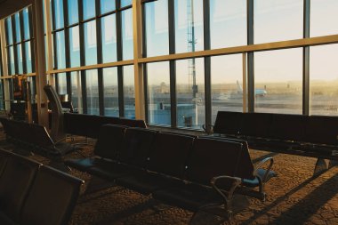 İçi boş, sessiz bir havaalanı terminali. Oturma sıraları ve büyük cam pencereler dışarıdaki pisti net bir şekilde gösteriyor.