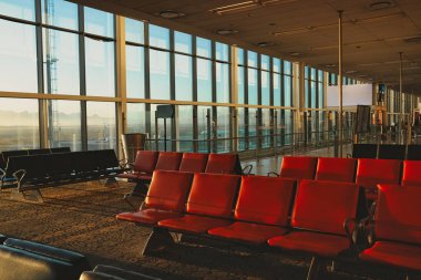 İçi boş, sessiz bir havaalanı terminali. Oturma sıraları ve büyük cam pencereler dışarıdaki pisti net bir şekilde gösteriyor.