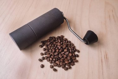 Hafif ahşap zemin üzerine serpiştirilmiş taze kahve çekirdekleri ile dokulu bir el yapımı kahve öğütücüsü.