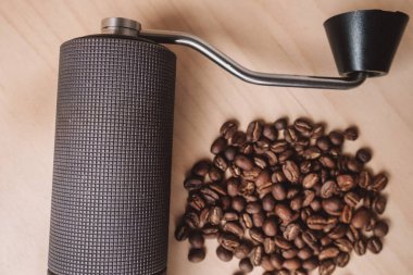 Hafif ahşap zemin üzerine serpiştirilmiş taze kahve çekirdekleri ile dokulu bir el yapımı kahve öğütücüsü.